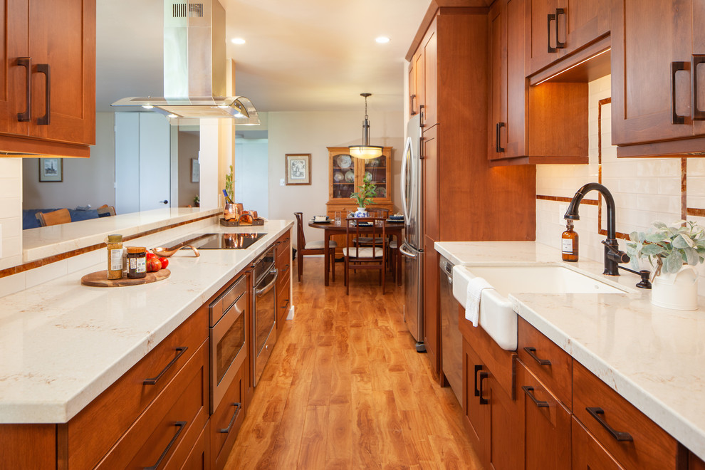 Inredning av ett retro mellanstort vit vitt kök, med en rustik diskho, skåp i shakerstil, bruna skåp, bänkskiva i kvarts, vitt stänkskydd, stänkskydd i keramik, rostfria vitvaror, mellanmörkt trägolv, en köksö och brunt golv