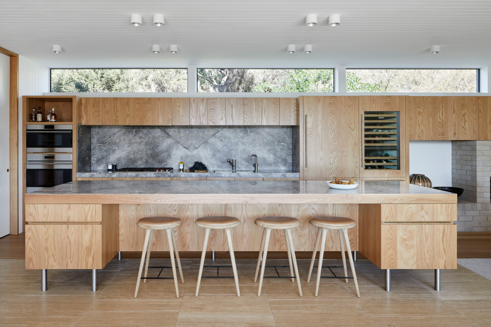 Inspiration for a large contemporary galley open plan kitchen in Melbourne with a submerged sink, flat-panel cabinets, medium wood cabinets, grey splashback, integrated appliances, an island, marble worktops, stone slab splashback, travertine flooring, beige floors and grey worktops.