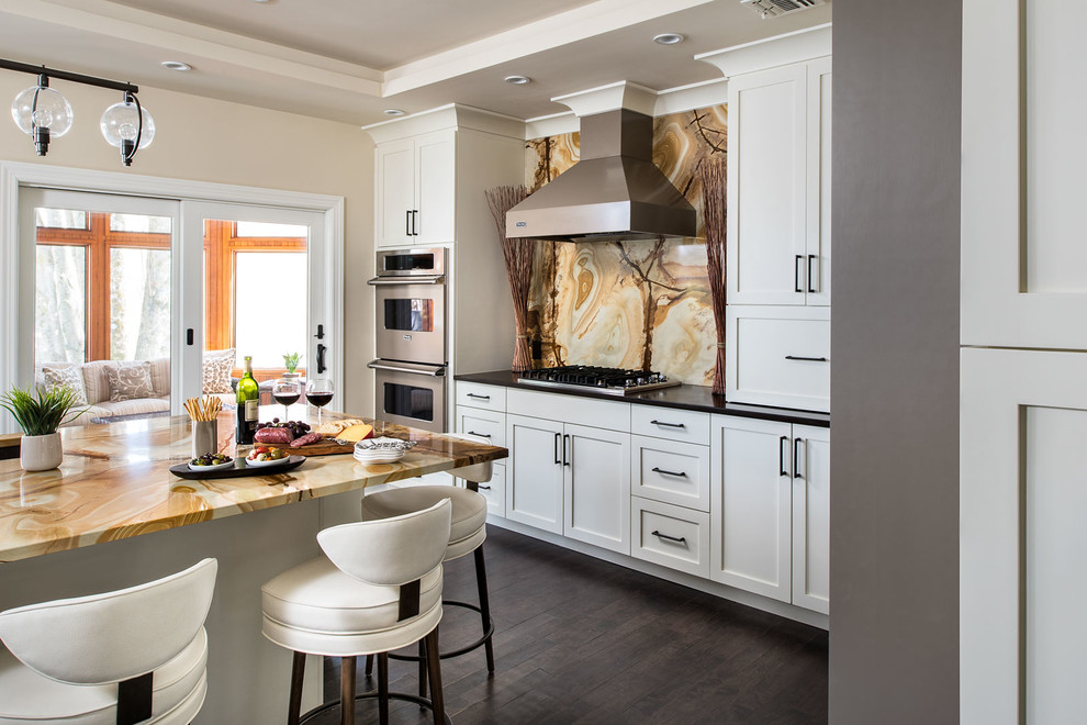 Example of a large transitional l-shaped dark wood floor eat-in kitchen design in New York with an undermount sink, shaker cabinets, white cabinets, granite countertops, multicolored backsplash, stone slab backsplash, stainless steel appliances and an island