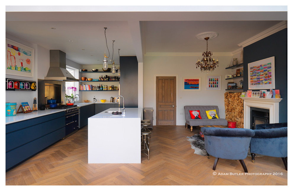 Bild på ett eklektiskt kök med öppen planlösning, med en enkel diskho, släta luckor, blå skåp, bänkskiva i täljsten, rostfria vitvaror, ljust trägolv och en köksö