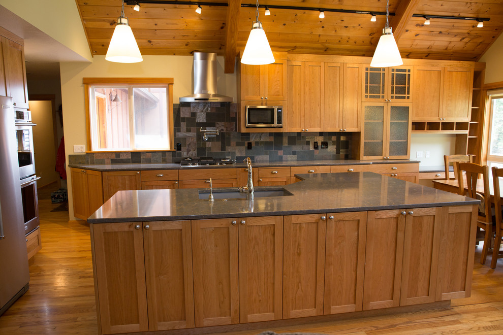 Foto på ett stort amerikanskt kök, med en undermonterad diskho, skåp i shakerstil, skåp i mellenmörkt trä, bänkskiva i kvarts, flerfärgad stänkskydd, stänkskydd i skiffer, rostfria vitvaror, mellanmörkt trägolv, en köksö och flerfärgat golv