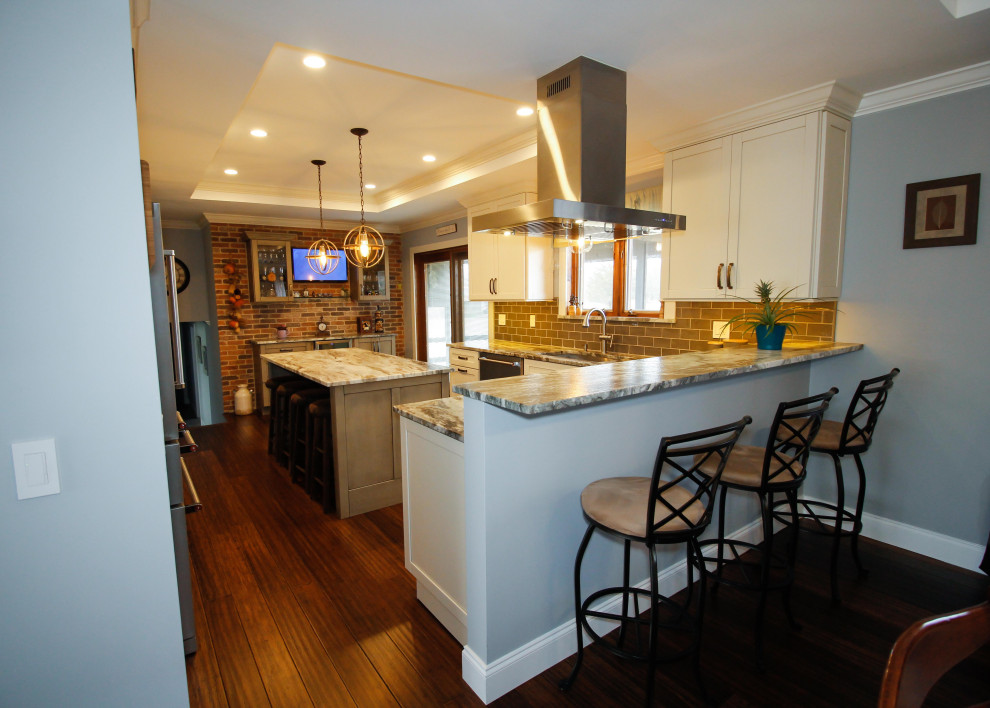 Example of a large trendy l-shaped bamboo floor, brown floor and tray ceiling eat-in kitchen design in New York with an undermount sink, recessed-panel cabinets, distressed cabinets, granite countertops, green backsplash, porcelain backsplash, stainless steel appliances, an island and multicolored countertops