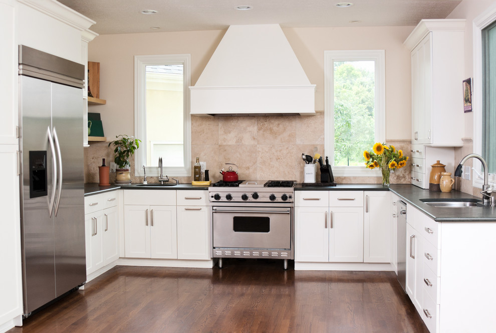 Klassisk inredning av ett mellanstort kök, med en dubbel diskho, skåp i shakerstil, vita skåp, bänkskiva i kvarts, beige stänkskydd, stänkskydd i sten, rostfria vitvaror och ljust trägolv