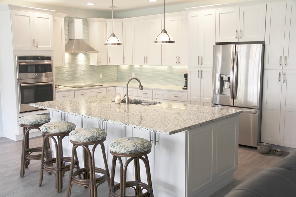 Mid-sized beach style l-shaped light wood floor and brown floor eat-in kitchen photo in Miami with an undermount sink, shaker cabinets, white cabinets, recycled glass countertops, green backsplash, glass tile backsplash, stainless steel appliances and an island