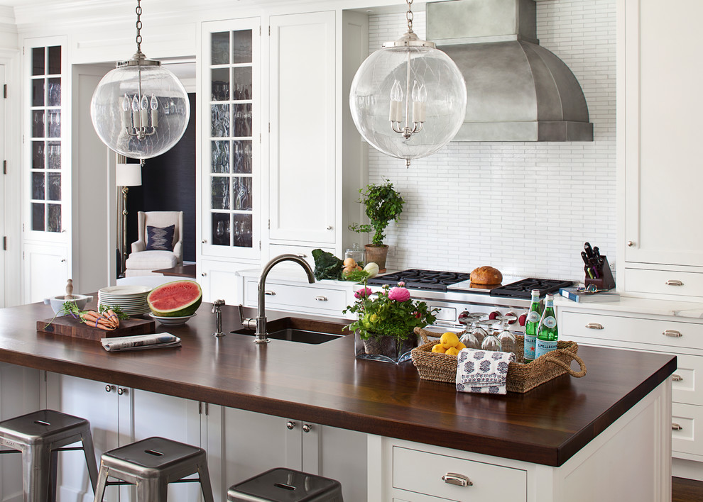 Klassisk inredning av ett kök, med vita skåp, träbänkskiva, stänkskydd i mosaik, en köksö, en undermonterad diskho, skåp i shakerstil och vitt stänkskydd