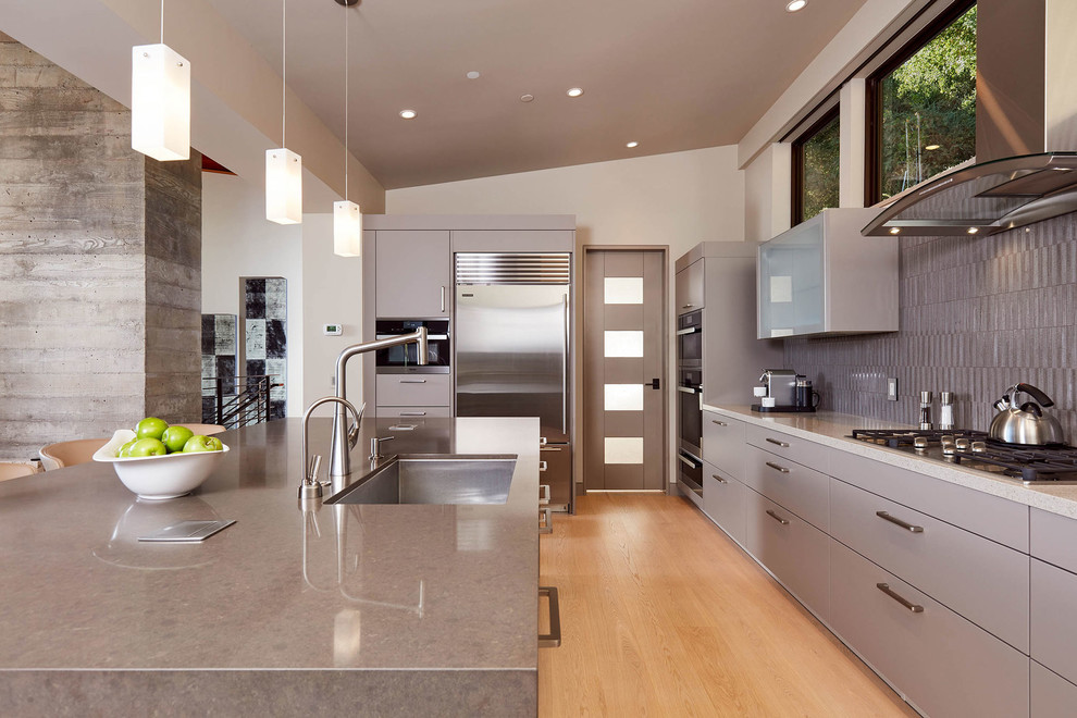 Large trendy u-shaped light wood floor and white floor eat-in kitchen photo in San Francisco with an undermount sink, flat-panel cabinets, gray cabinets, quartz countertops, gray backsplash, ceramic backsplash, stainless steel appliances and an island