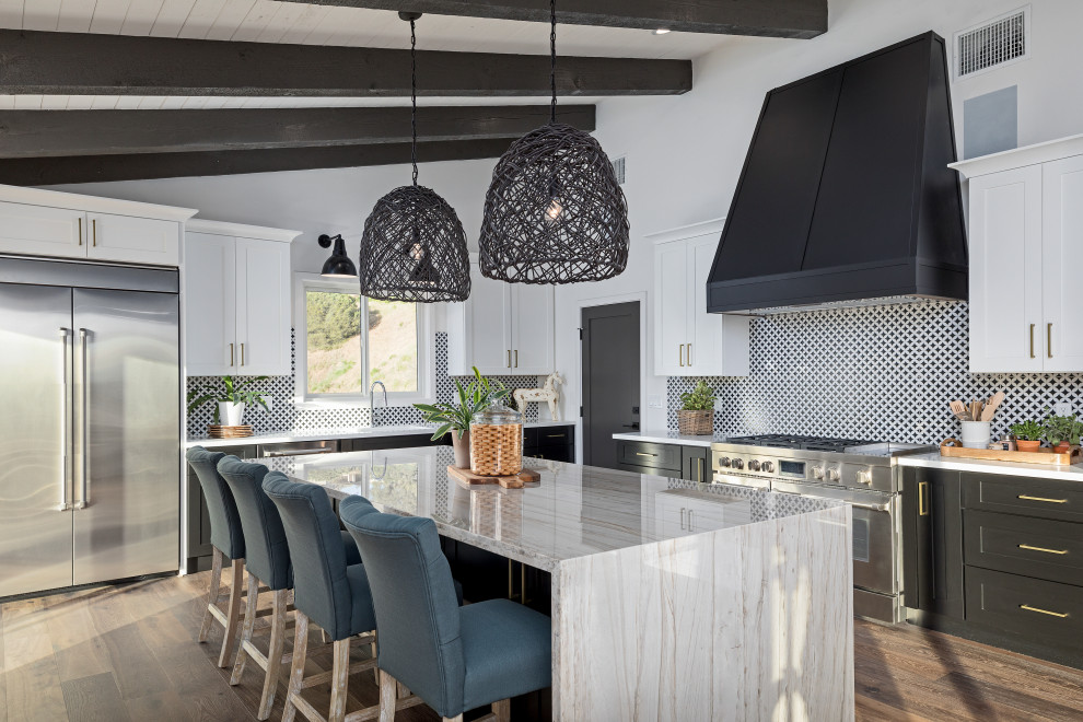 Design ideas for a large traditional l-shaped kitchen/diner in Los Angeles with a submerged sink, shaker cabinets, black cabinets, engineered stone countertops, white splashback, porcelain splashback, stainless steel appliances, medium hardwood flooring, an island, beige floors and beige worktops.