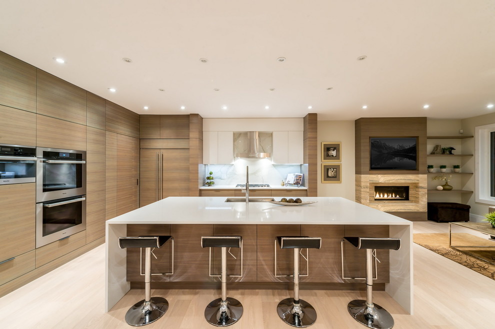 Large trendy l-shaped light wood floor open concept kitchen photo in Vancouver with an undermount sink, flat-panel cabinets, light wood cabinets, solid surface countertops, white backsplash, stone slab backsplash, stainless steel appliances and an island