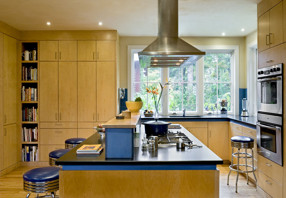 Modelo de cocina actual con electrodomésticos de acero inoxidable, armarios con paneles lisos, puertas de armario de madera oscura y barras de cocina