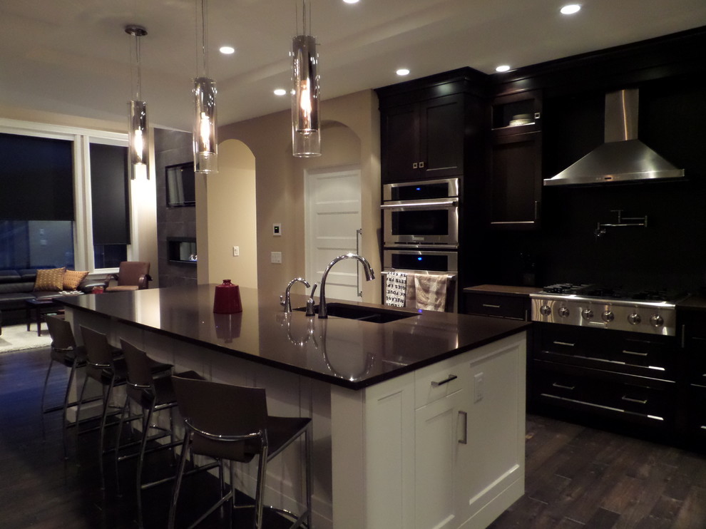 Modern inredning av ett mellanstort kök, med en undermonterad diskho, skåp i shakerstil, vita skåp, bänkskiva i kvartsit, svart stänkskydd, stänkskydd i marmor, rostfria vitvaror, mörkt trägolv, en köksö och brunt golv