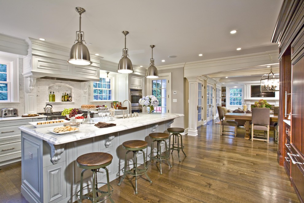 Example of a large classic dark wood floor open concept kitchen design in New York with raised-panel cabinets, an undermount sink, white cabinets, marble countertops, gray backsplash, stone tile backsplash, paneled appliances and an island