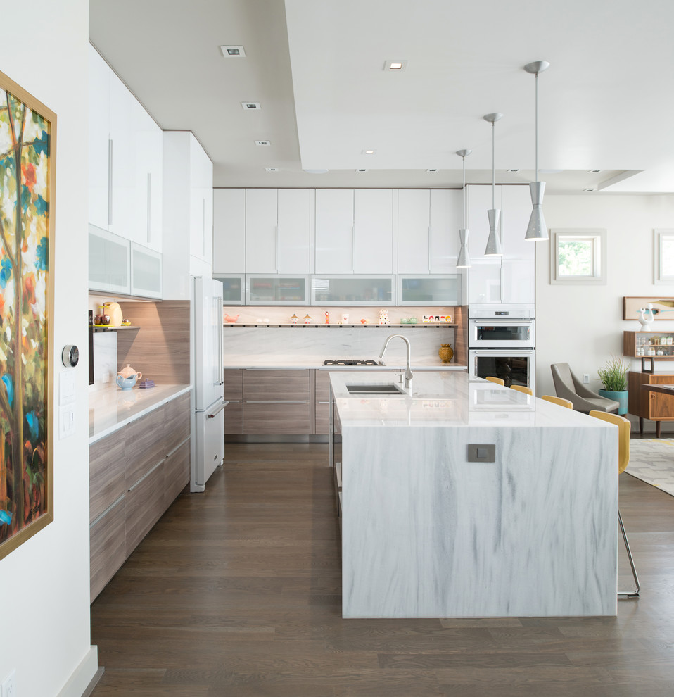 Inspiration for a modern l-shaped open plan kitchen in Kansas City with a submerged sink, flat-panel cabinets, white cabinets, marble worktops, white splashback, white appliances, light hardwood flooring and an island.