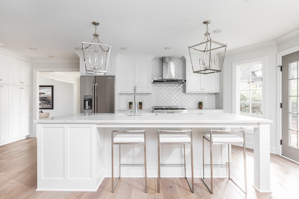 Example of a large transitional single-wall light wood floor and brown floor open concept kitchen design in Indianapolis with shaker cabinets, white cabinets, white backsplash, stainless steel appliances, an island, an undermount sink, quartz countertops and white countertops