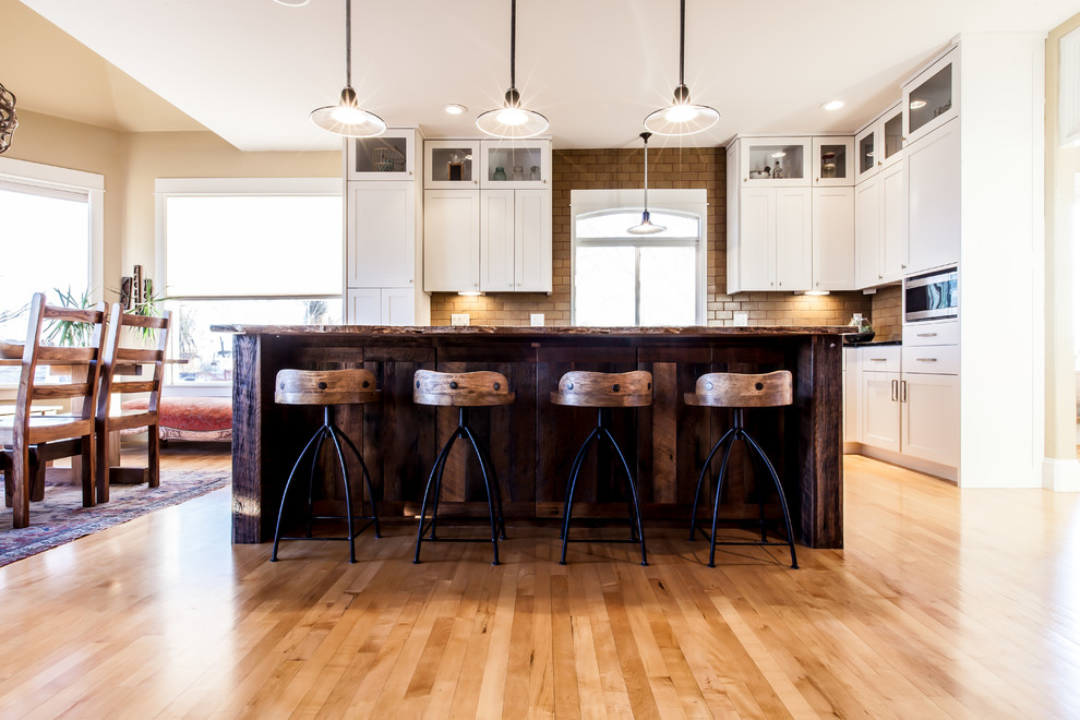 Mid-sized cottage l-shaped light wood floor and yellow floor eat-in kitchen photo in Denver with a farmhouse sink, flat-panel cabinets, medium tone wood cabinets, soapstone countertops, green backsplash, ceramic backsplash, stainless steel appliances, an island and black countertops