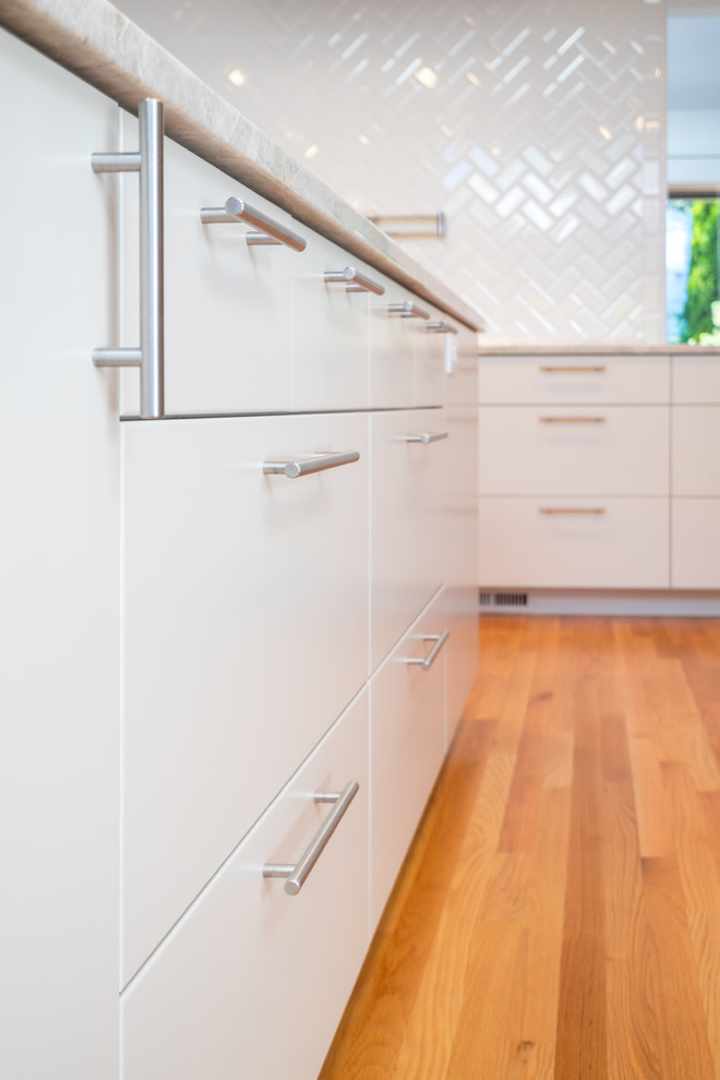 Inspiration for a large transitional l-shaped medium tone wood floor open concept kitchen remodel in Portland with an undermount sink, flat-panel cabinets, white cabinets, quartzite countertops, white backsplash, ceramic backsplash, stainless steel appliances and an island