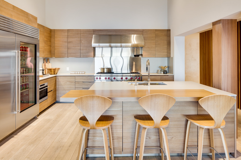 This is an example of a contemporary l-shaped kitchen in Miami with a submerged sink, flat-panel cabinets, light wood cabinets, metallic splashback, stainless steel appliances, light hardwood flooring and an island.