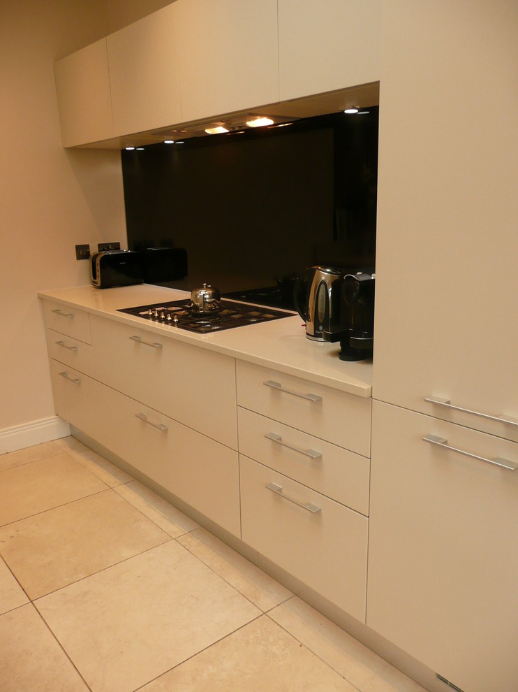 This is an example of a medium sized contemporary galley kitchen/diner in Dublin with a submerged sink, flat-panel cabinets, grey cabinets, engineered stone countertops, black splashback, glass sheet splashback, stainless steel appliances, ceramic flooring and a breakfast bar.