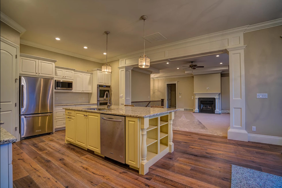 Exempel på ett stort klassiskt l-kök, med en undermonterad diskho, luckor med upphöjd panel, vita skåp, granitbänkskiva, vitt stänkskydd, stänkskydd i tunnelbanekakel, rostfria vitvaror, mellanmörkt trägolv, en köksö och brunt golv