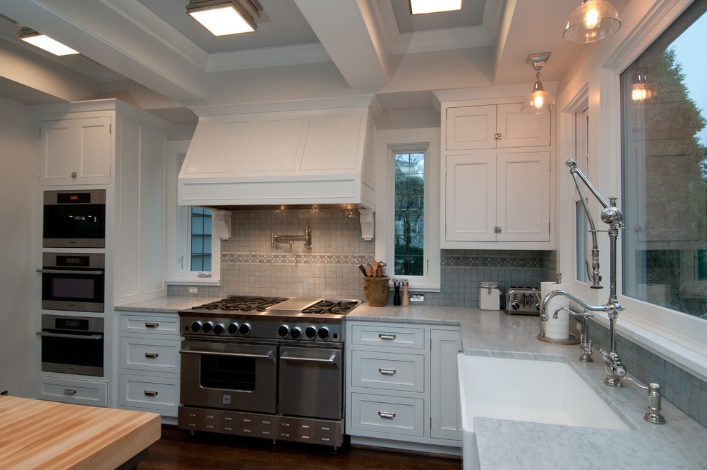 Diseño de cocina clásica con electrodomésticos de acero inoxidable, fregadero sobremueble, armarios con paneles empotrados, puertas de armario blancas, encimera de mármol y salpicadero azul