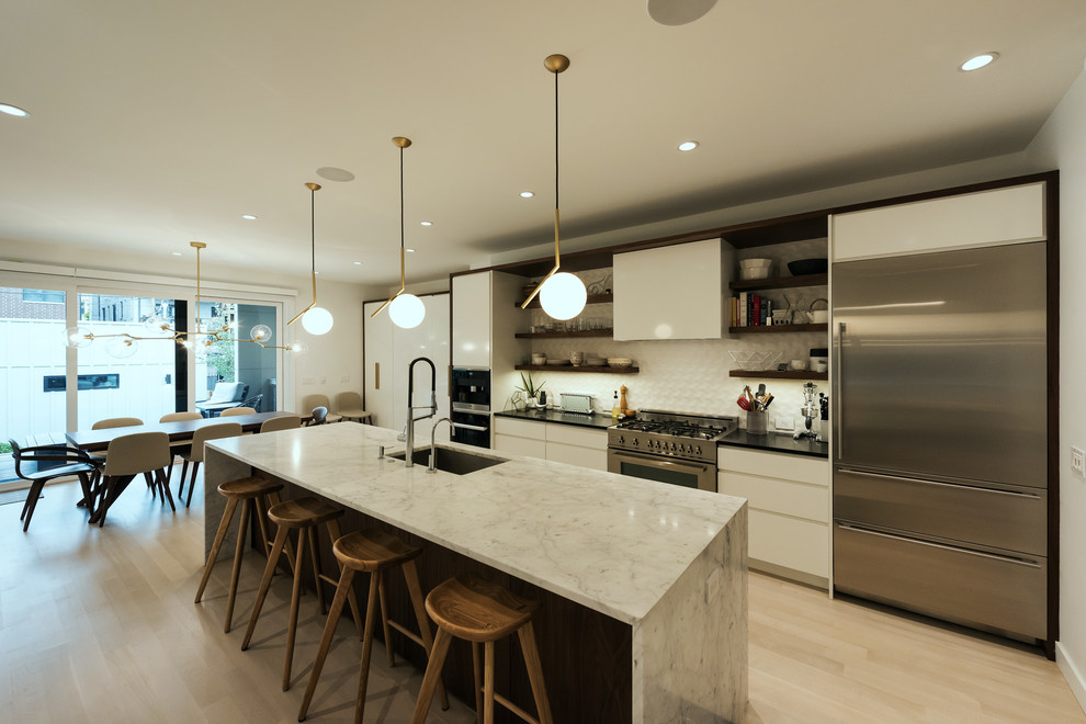 Example of a large minimalist galley light wood floor and white floor eat-in kitchen design in Chicago with an undermount sink, flat-panel cabinets, white cabinets, quartz countertops, white backsplash, porcelain backsplash, stainless steel appliances and an island