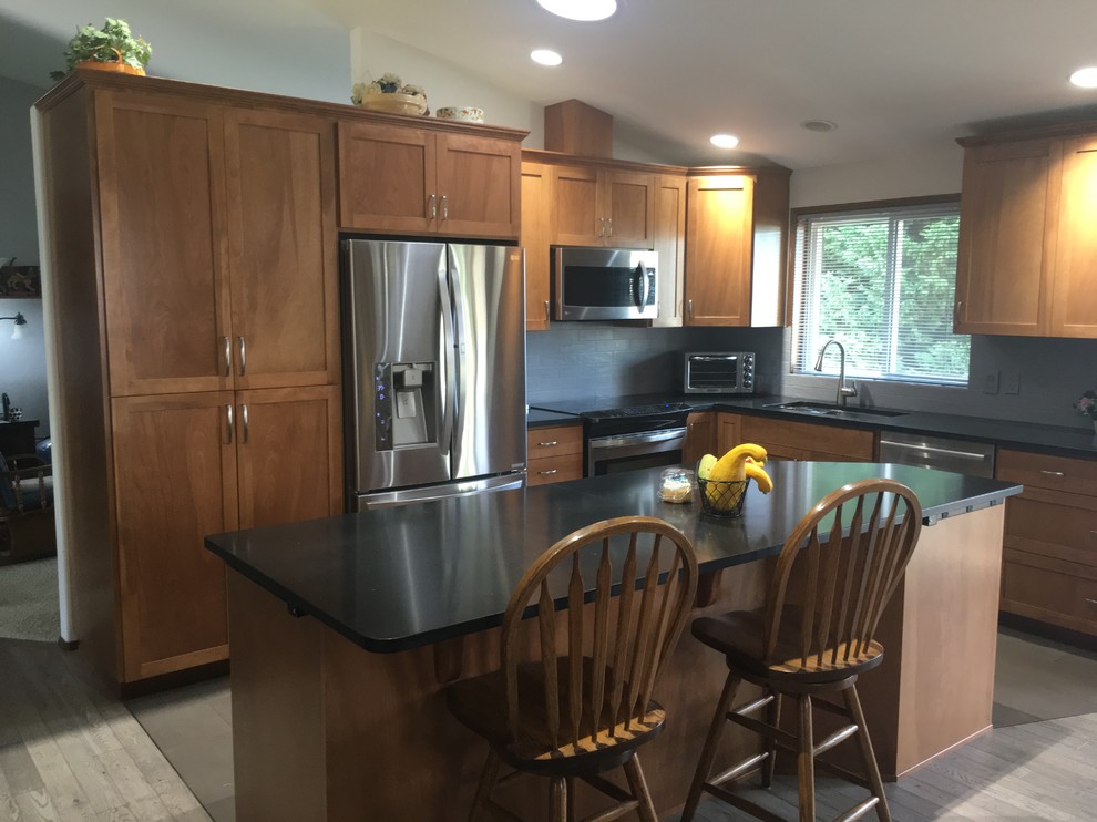 Bild på ett mellanstort funkis kök, med en undermonterad diskho, skåp i shakerstil, skåp i mellenmörkt trä, bänkskiva i kvarts, blått stänkskydd, stänkskydd i tegel, rostfria vitvaror, ljust trägolv och en köksö