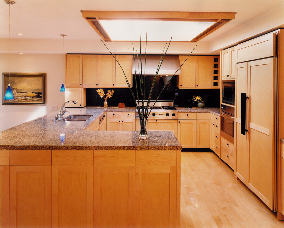 Exempel på ett stort modernt brun brunt kök, med en dubbel diskho, skåp i shakerstil, skåp i ljust trä, granitbänkskiva, svart stänkskydd, rostfria vitvaror, ljust trägolv, en halv köksö, stänkskydd i sten och gult golv