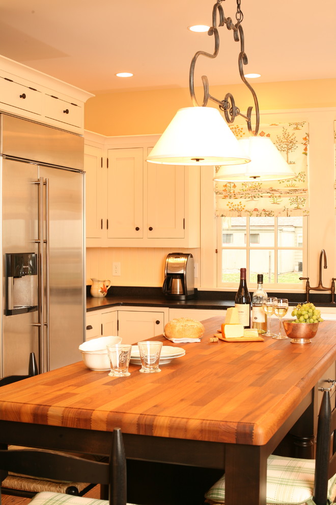 Imagen de cocina tradicional con electrodomésticos de acero inoxidable, encimera de madera, puertas de armario blancas y barras de cocina