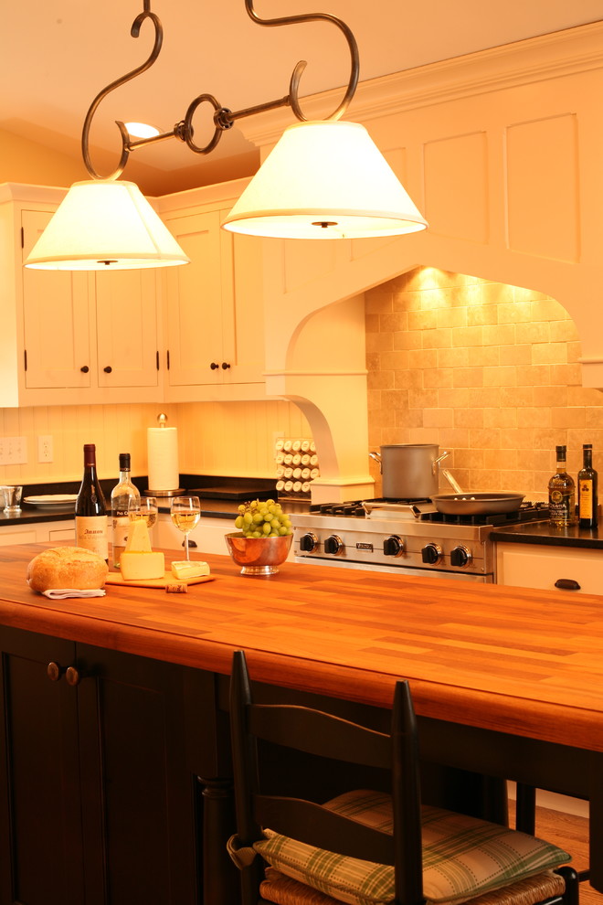 Cette image montre une cuisine traditionnelle avec un placard à porte shaker, des portes de placard beiges, un plan de travail en bois, une crédence beige et un électroménager en acier inoxydable.