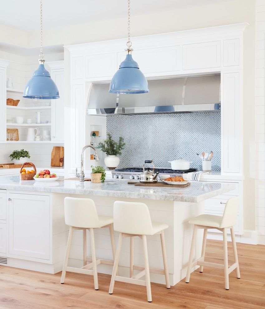 Foto de cocina costera con suelo de madera clara, una isla, armarios estilo shaker, puertas de armario blancas, salpicadero azul y suelo marrón