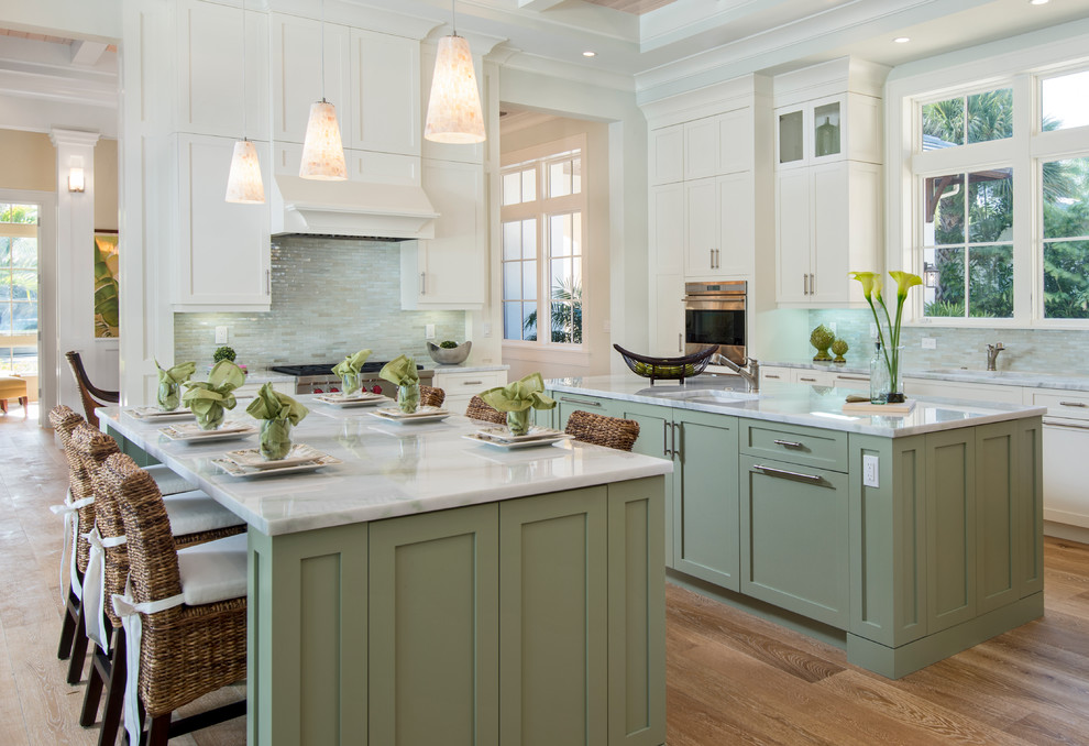 Inspiration for a classic kitchen in Other with a submerged sink, shaker cabinets, green cabinets, grey splashback, glass tiled splashback, stainless steel appliances, light hardwood flooring and multiple islands.