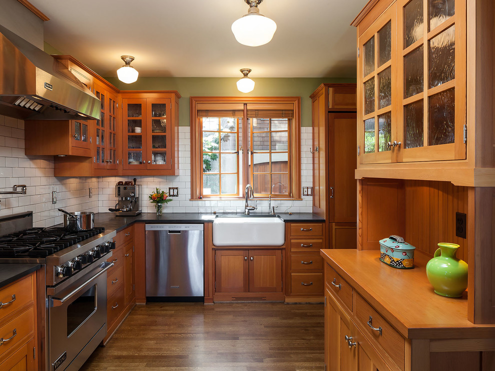 Foto på ett amerikanskt kök, med en rustik diskho, luckor med profilerade fronter, skåp i mellenmörkt trä, vitt stänkskydd, stänkskydd i tunnelbanekakel, rostfria vitvaror och mellanmörkt trägolv