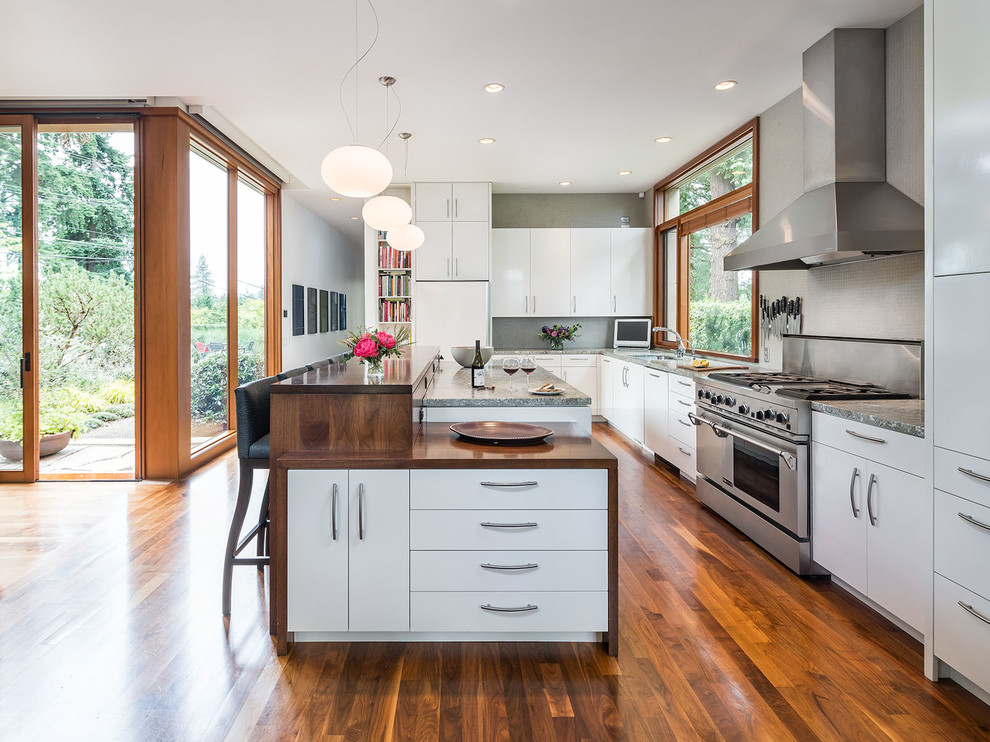 Moderne Küche in L-Form mit flächenbündigen Schrankfronten, weißen Schränken, Küchengeräten aus Edelstahl, braunem Holzboden, Unterbauwaschbecken und zwei Kücheninseln in Portland