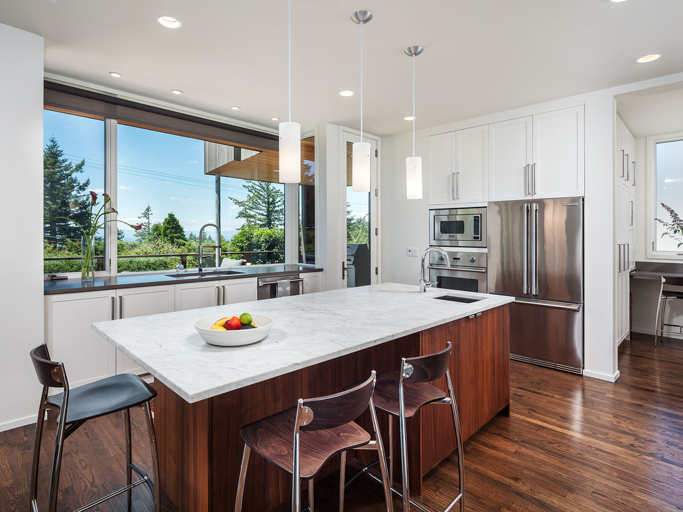 Moderne Küche mit Unterbauwaschbecken, Schrankfronten im Shaker-Stil, weißen Schränken, Küchengeräten aus Edelstahl, braunem Holzboden und Kücheninsel in Portland