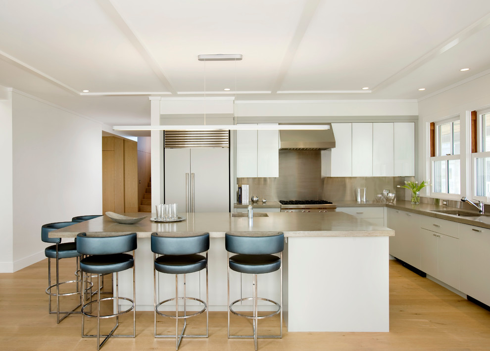 Foto på ett funkis l-kök, med släta luckor, vita skåp, bänkskiva i betong, stänkskydd med metallisk yta, rostfria vitvaror och stänkskydd i metallkakel