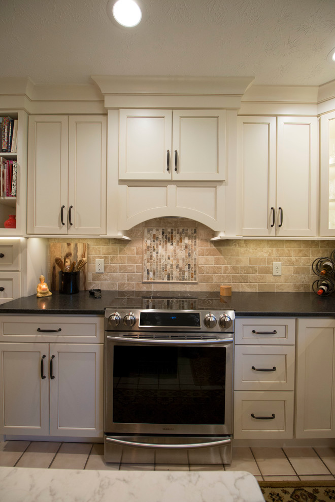 Example of a mid-sized classic u-shaped porcelain tile enclosed kitchen design in Other with an undermount sink, recessed-panel cabinets, white cabinets, granite countertops, beige backsplash, stone tile backsplash, stainless steel appliances and an island