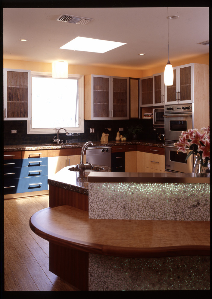 Пример оригинального дизайна: угловая кухня-гостиная среднего размера в современном стиле с одинарной мойкой, стеклянными фасадами, светлыми деревянными фасадами, столешницей из переработанного стекла, черным фартуком, техникой из нержавеющей стали, полом из бамбука и островом