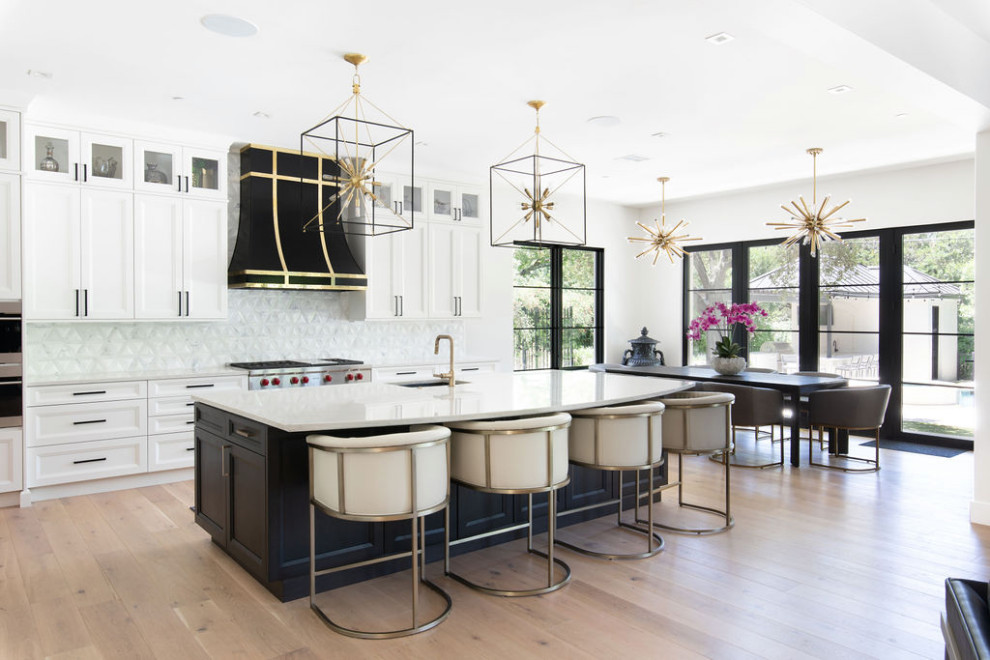 Example of a large transitional l-shaped light wood floor open concept kitchen design in Austin with shaker cabinets, white cabinets, quartzite countertops, white backsplash, marble backsplash, stainless steel appliances, an island and white countertops