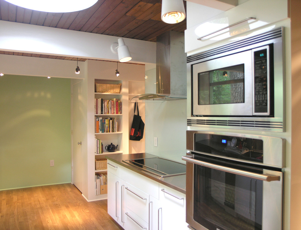 フィラデルフィアにあるコンテンポラリースタイルのおしゃれなII型キッチン (フラットパネル扉のキャビネット、ステンレスカウンター、シルバーの調理設備、無垢フローリング、ガラス板のキッチンパネル) の写真