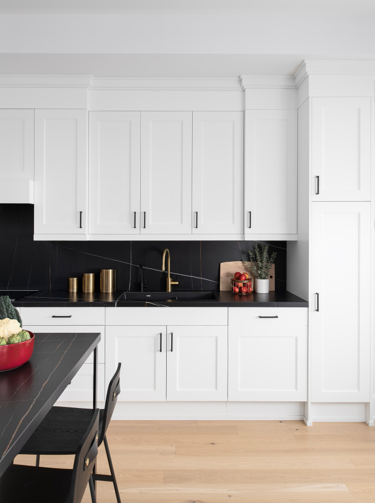 Idéer för ett mellanstort nordiskt svart kök, med en undermonterad diskho, skåp i shakerstil, vita skåp, svart stänkskydd, vita vitvaror, ljust trägolv och en halv köksö