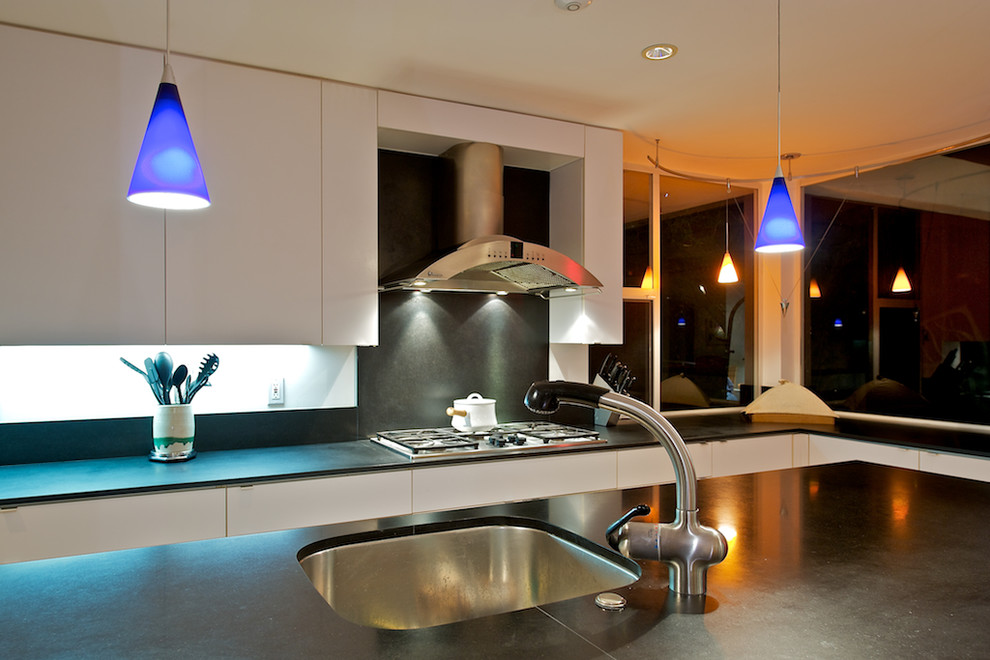 Example of a minimalist l-shaped eat-in kitchen design in Los Angeles with an undermount sink, flat-panel cabinets, white cabinets, soapstone countertops, stainless steel appliances, an island and black countertops
