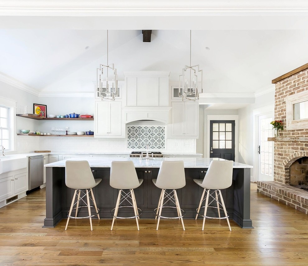 Klassische Küche in L-Form mit Landhausspüle, Schrankfronten im Shaker-Stil, weißen Schränken, Küchenrückwand in Weiß, Küchengeräten aus Edelstahl, braunem Holzboden, Kücheninsel, braunem Boden und weißer Arbeitsplatte in Charleston
