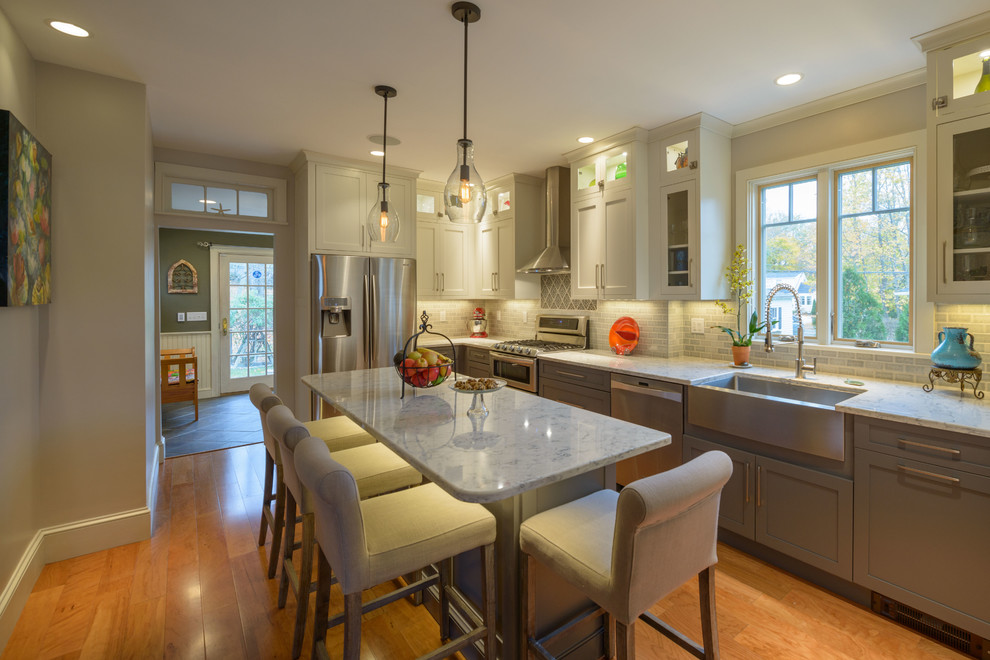 Eat-in kitchen - mid-sized transitional l-shaped light wood floor eat-in kitchen idea in Boston with a farmhouse sink, shaker cabinets, gray cabinets, quartz countertops, ceramic backsplash, an island and gray backsplash