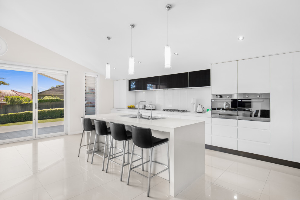 Zweizeilige Moderne Küche mit Einbauwaschbecken, flächenbündigen Schrankfronten, weißen Schränken, Elektrogeräten mit Frontblende, Kücheninsel, beigem Boden und weißer Arbeitsplatte in Sydney