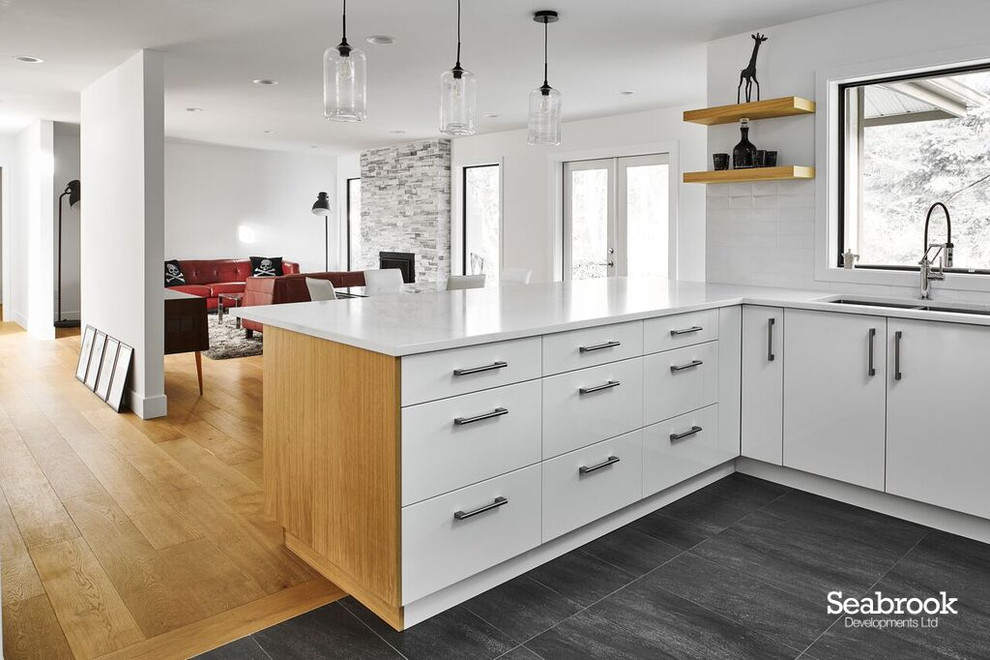 Medium sized contemporary u-shaped kitchen/diner in Vancouver with a submerged sink, flat-panel cabinets, white cabinets, engineered stone countertops, white splashback, ceramic splashback, stainless steel appliances, slate flooring, a breakfast bar, black floors and white worktops.