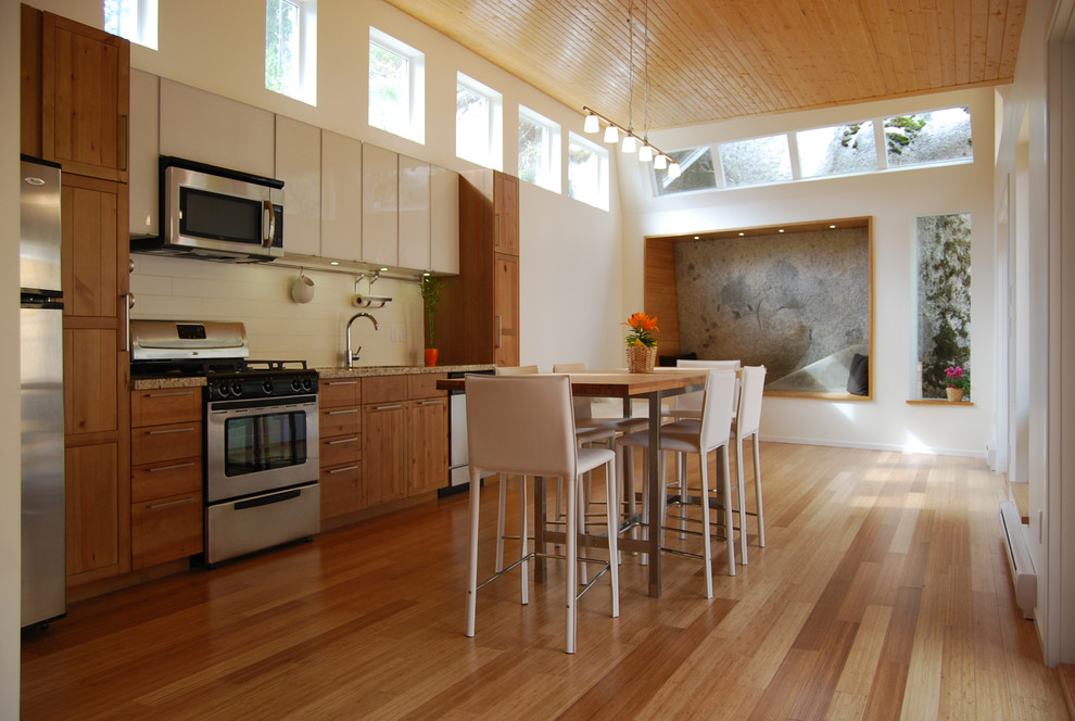 Modelo de cocina lineal moderna pequeña con puertas de armario de madera oscura, salpicadero blanco, salpicadero de azulejos tipo metro, electrodomésticos de acero inoxidable, armarios estilo shaker, encimera de granito, suelo de bambú y una isla