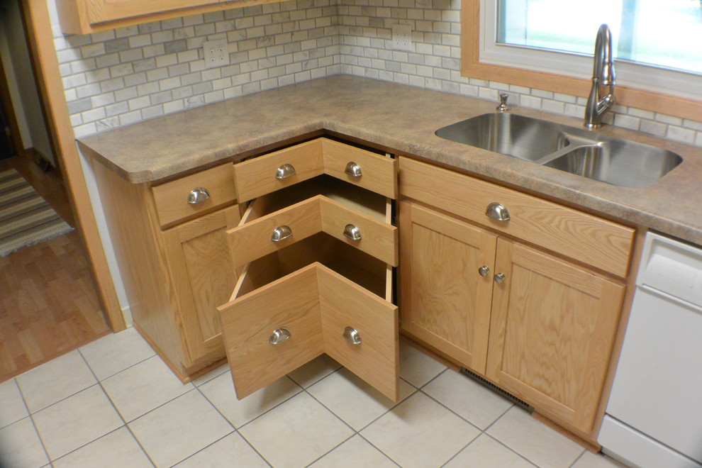 Example of a classic l-shaped eat-in kitchen design in Minneapolis with an undermount sink, flat-panel cabinets, light wood cabinets, laminate countertops, gray backsplash and white appliances