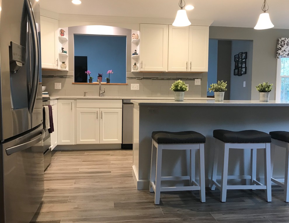 Medium sized classic l-shaped open plan kitchen in Boston with a single-bowl sink, flat-panel cabinets, white cabinets, engineered stone countertops, grey splashback, metro tiled splashback, stainless steel appliances, porcelain flooring, an island, grey floors and white worktops.