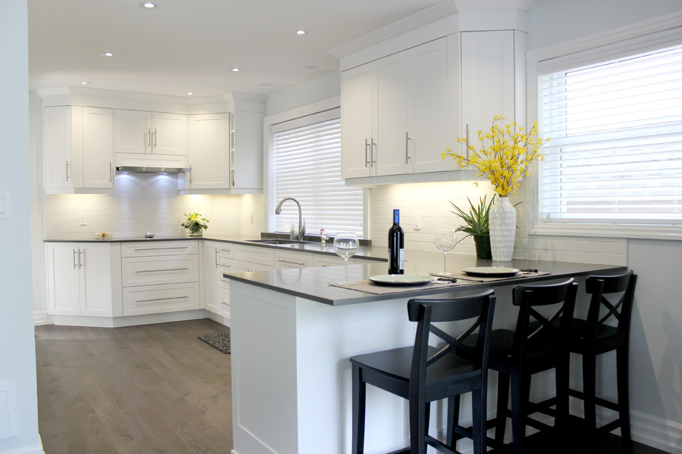 Exempel på ett modernt kök, med en undermonterad diskho, skåp i shakerstil, vita skåp, bänkskiva i kvarts, vitt stänkskydd, stänkskydd i tunnelbanekakel, rostfria vitvaror, mellanmörkt trägolv och en halv köksö