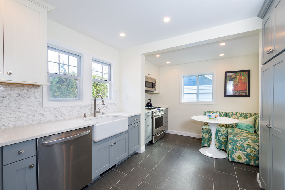 Traditional grey and white galley kitchen/diner in New York with a belfast sink, shaker cabinets, engineered stone countertops, white splashback, stone tiled splashback, stainless steel appliances, grey floors and grey cabinets.