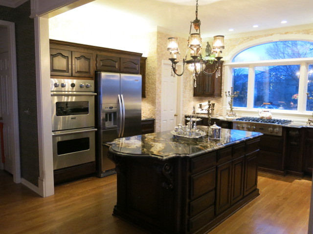 This is an example of a large traditional u-shaped kitchen/diner in Kansas City with a submerged sink, recessed-panel cabinets, dark wood cabinets, granite worktops, white splashback, stone tiled splashback, stainless steel appliances, light hardwood flooring and an island.